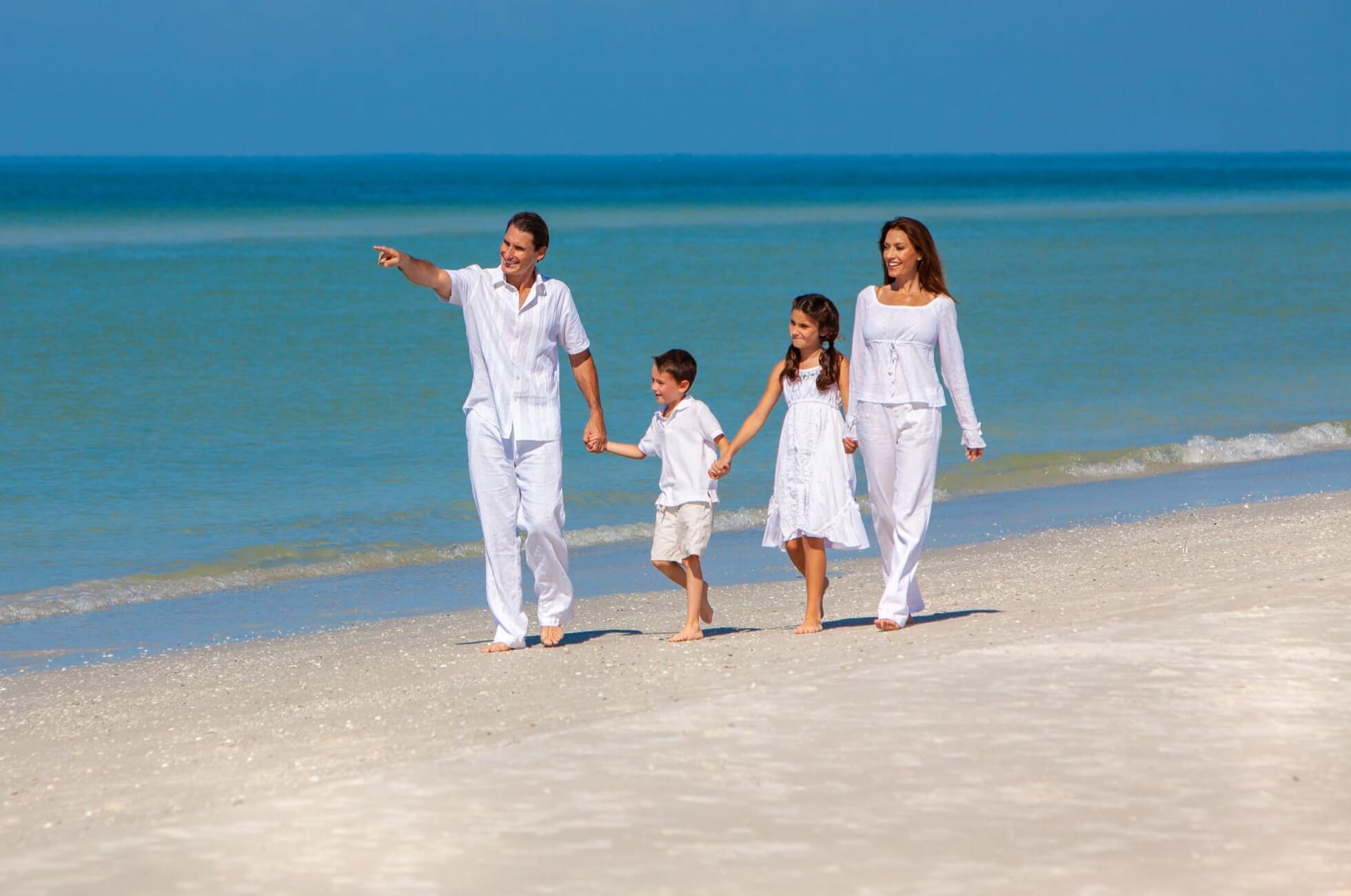 Wealthy family dressed in white walking on the beach