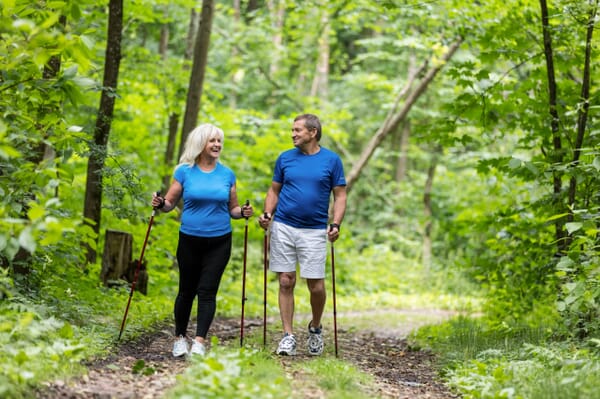 Older couple walking on path in the woods with walking poles