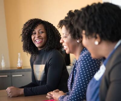 Three professional black women smiling and talking at a table