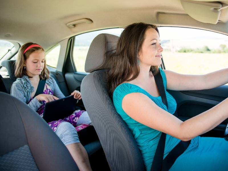 Mother driving and smiling at adolescent daughter in back seat