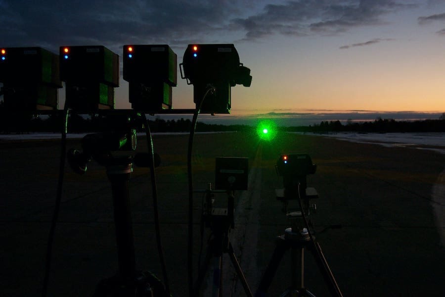 Bank of four laser sensors outdoors at night with green beam visible