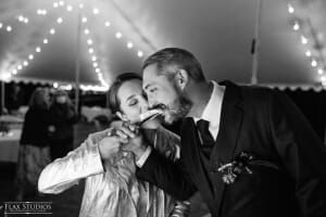 Black and white image of bride feeding groom cake at Maine wedding under tent lights