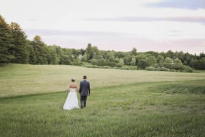 Newlywed couple walking away through a meadow