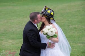 Groom kissing bride wearing firefighter helmet