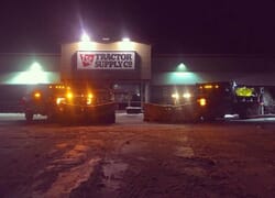 Snow plowing trucks at night in front of a lighted Tractor Supply Co building