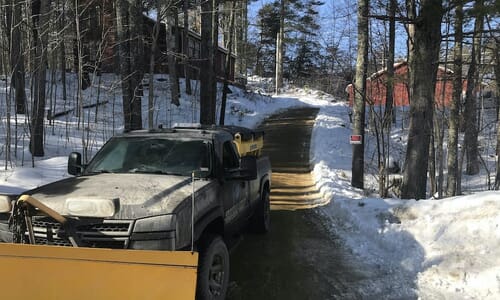 Truck with plow at the end of a long driveway in winter