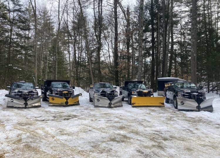 Snow plowing trucks parked in a line on a winter day in front of the woods